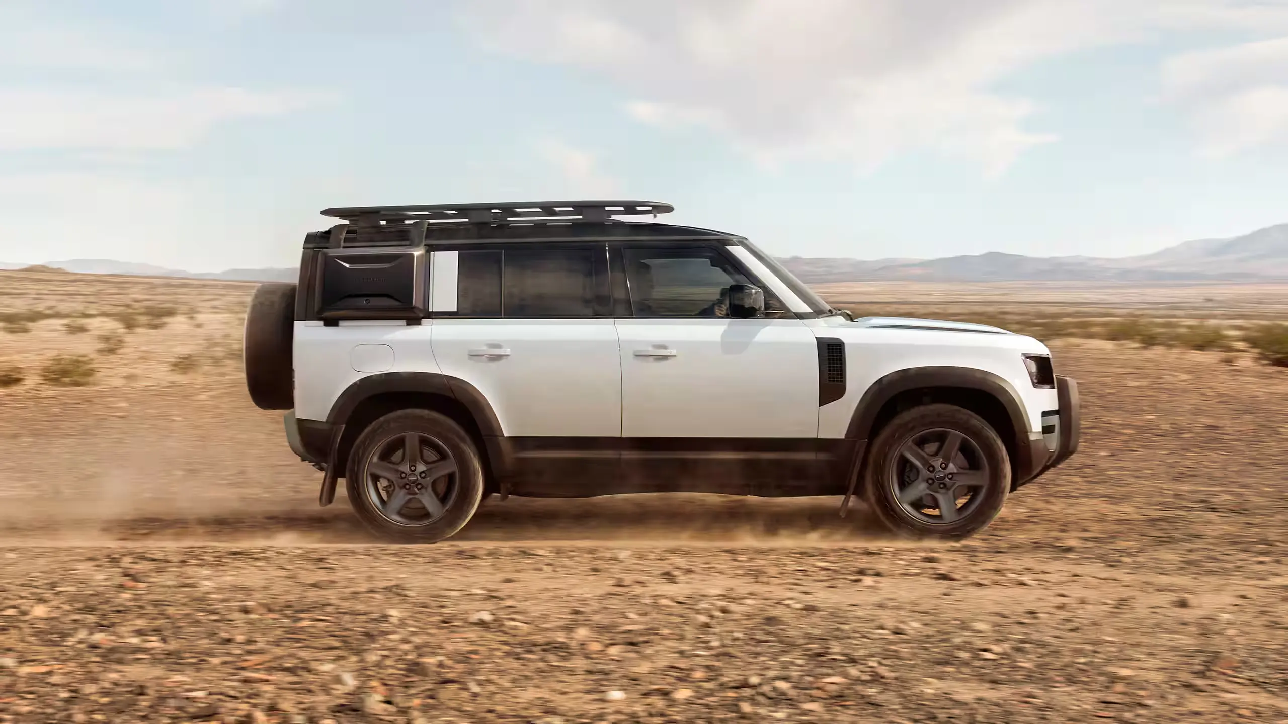 White Defender 110 with expedition accessories traveling across open terrain