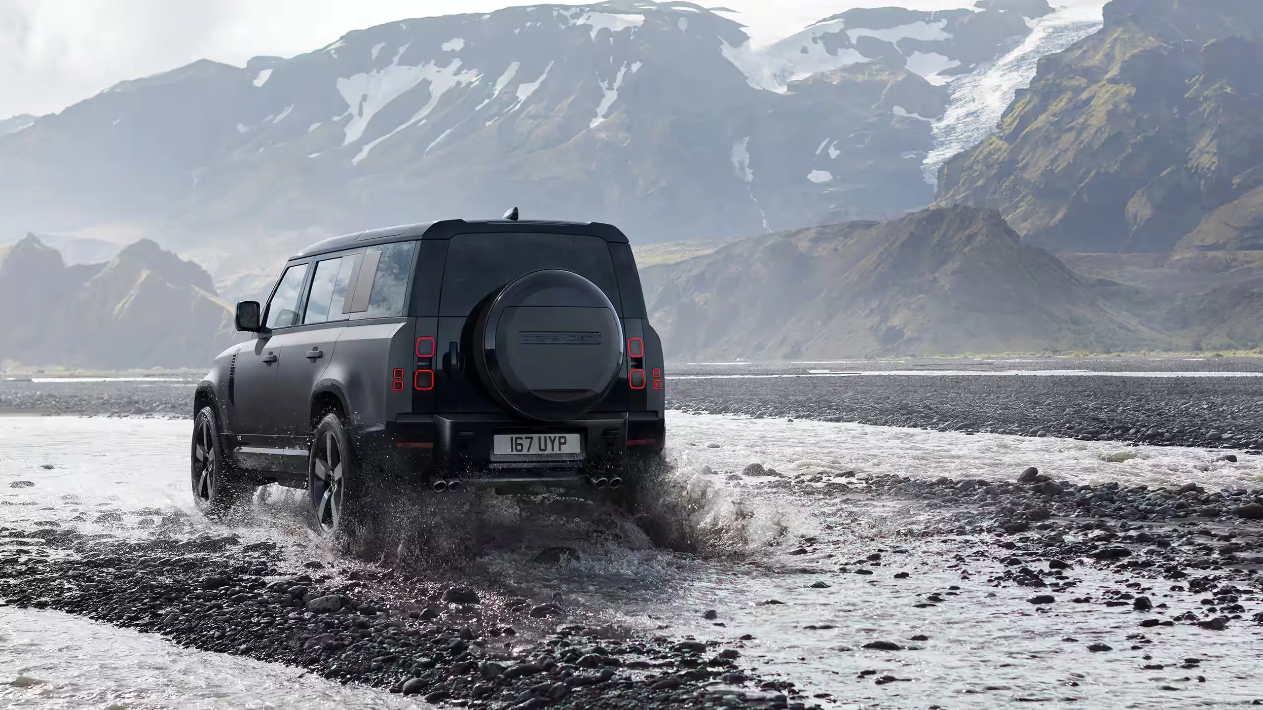 Defender 110 crossing shallow water in a mountain landscape