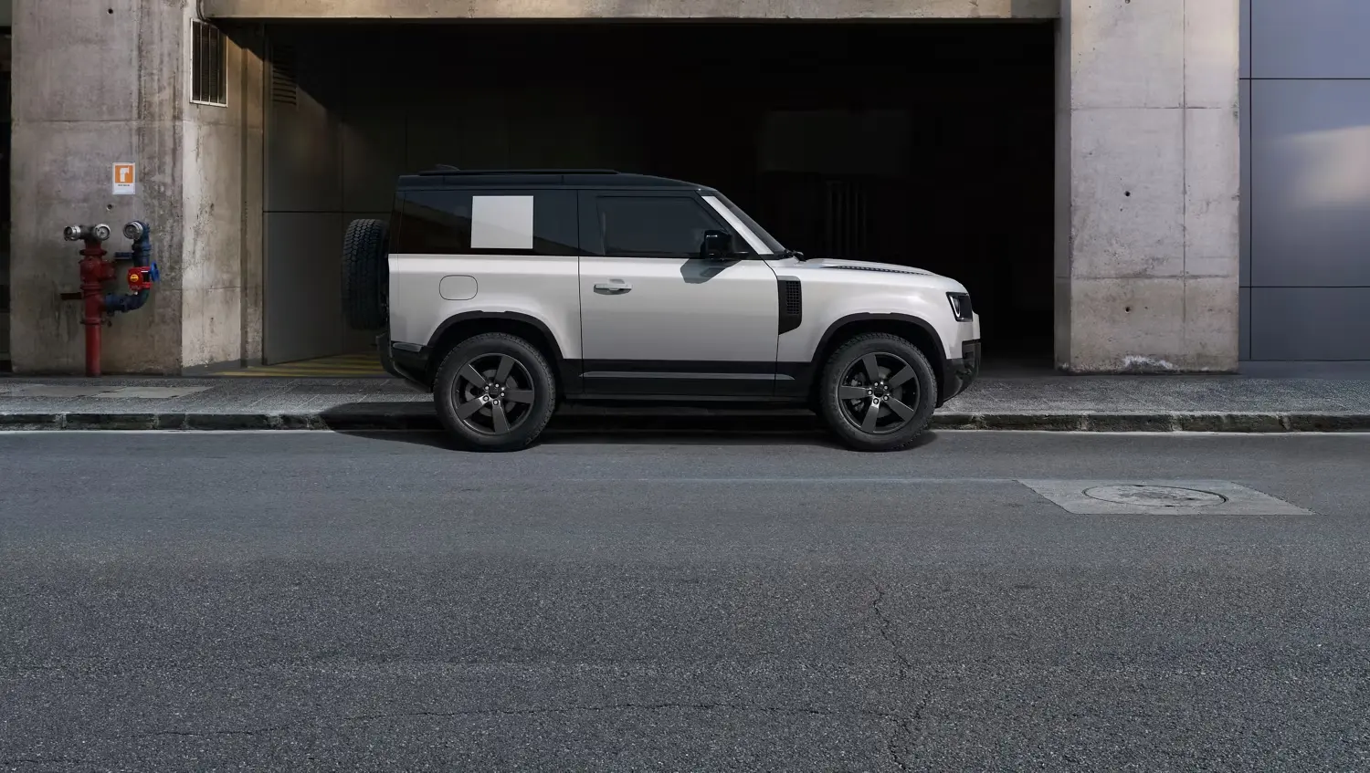 White two-door Defender 90 in profile outside a modern building