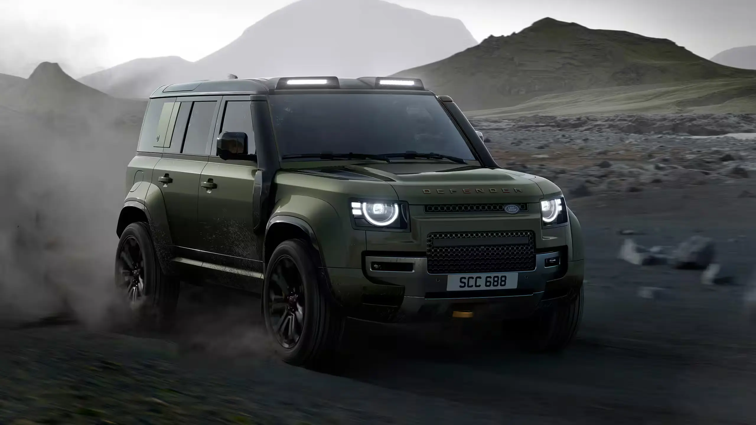 Green Defender OCTA driving quickly across dark off-road terrain