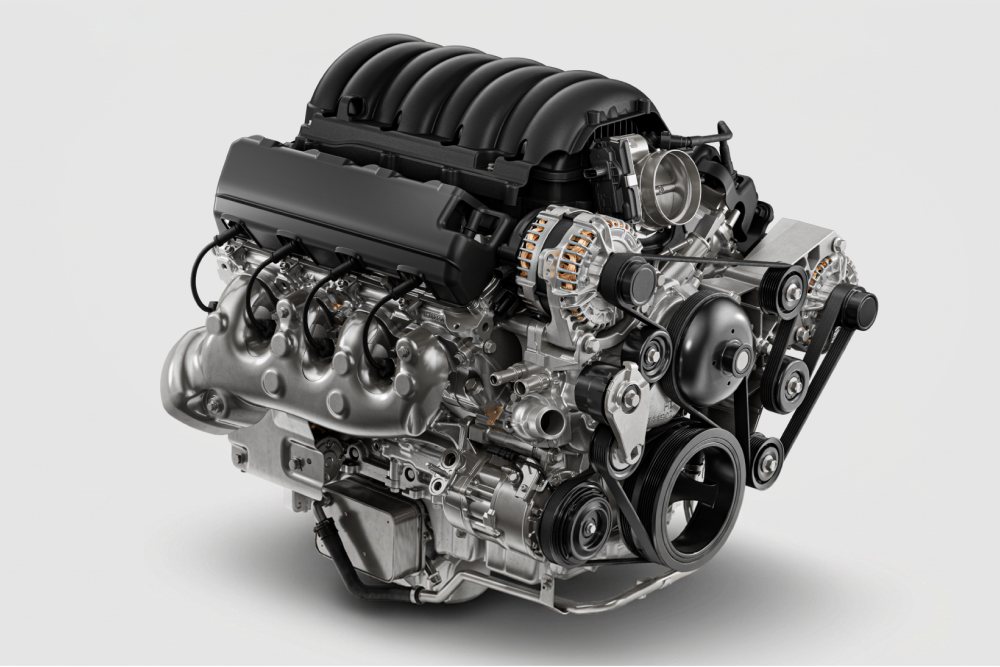 Studio render of a V8 engine with a black intake cover and exposed exhaust manifold, on a white background