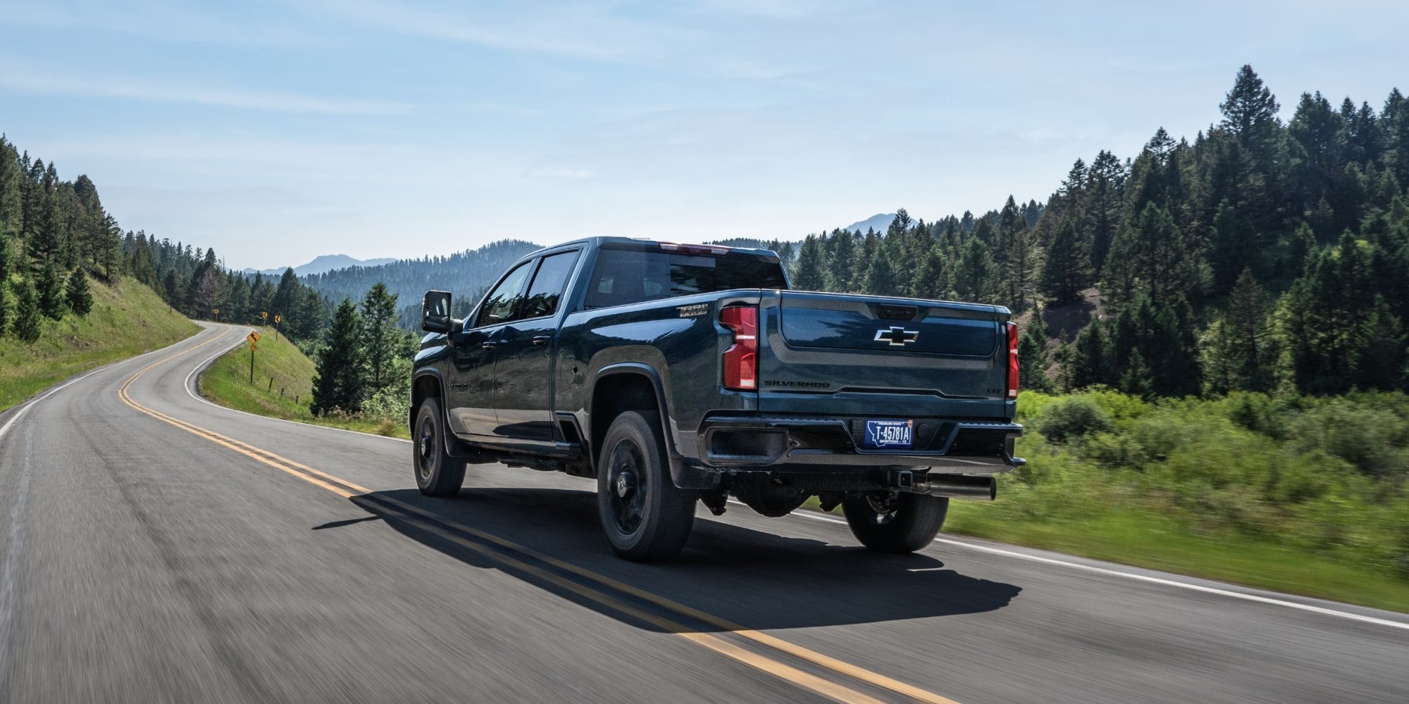 Dark blue Chevrolet Silverado HD driving away on a winding two-lane road through pine forest