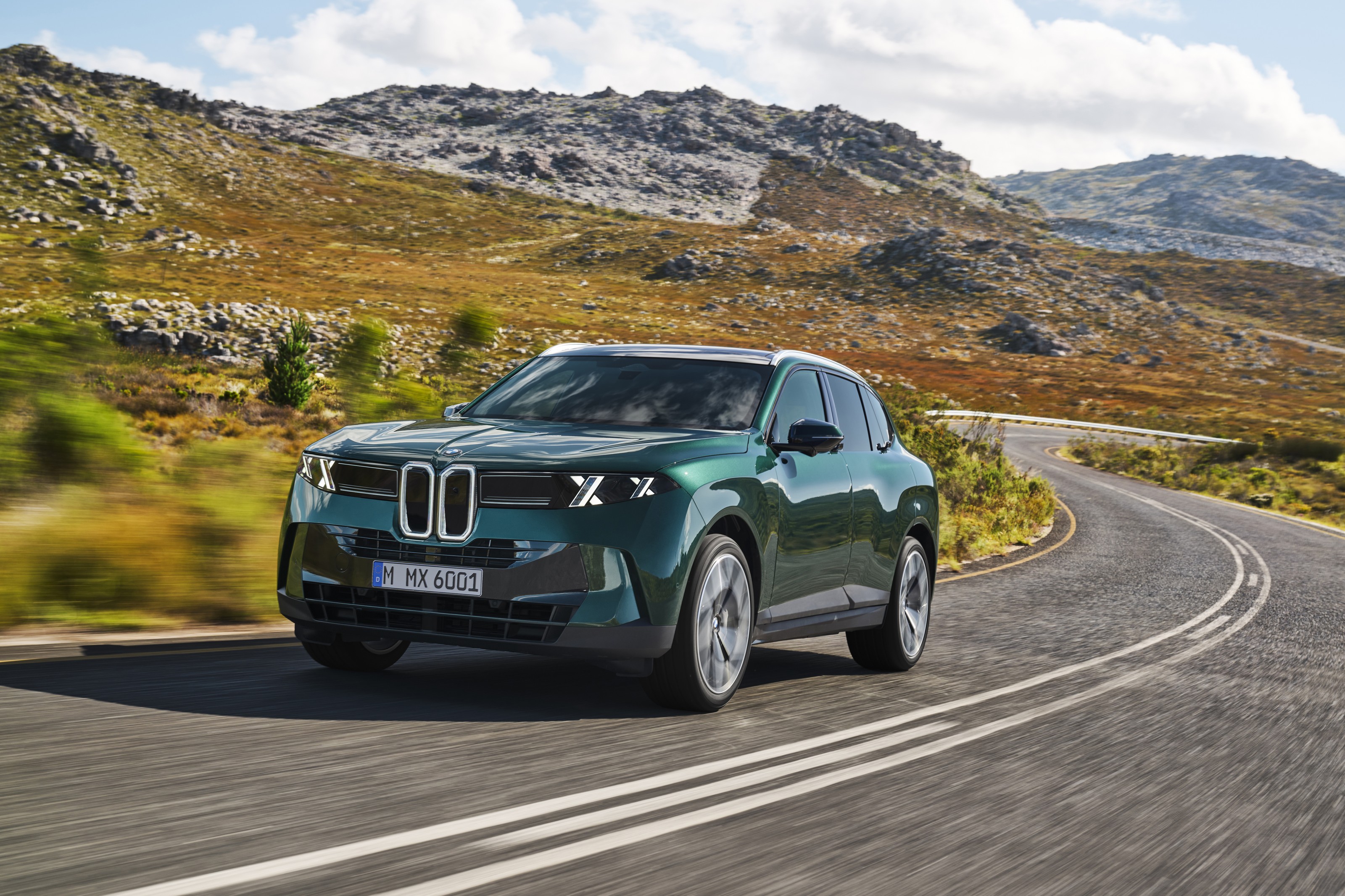 Dark green 2027 BMW X5 driving toward the camera on a curving mountain road